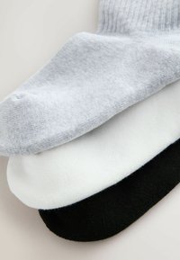 Trzy pary skarpetek w kolorach szarym, białym i czarnym. Każda skarpetka charakteryzuje się gładką teksturą i prążkowanym ściągaczem dla większego komfortu i dopasowania.