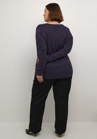 Bluza lungă mov cu un croi lejer, decolteu rotund și textură moale, purtată împreună cu pantaloni negri cu picioare largi.