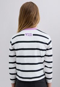 Camisa de manga larga a rayas en blanco y negro con un cuello morado. Presenta una etiqueta cuadrada en la parte posterior con "SCALPERS" en texto morado.
