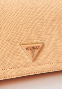 Peach-colored textured clutch with a triangular gold hardware logo featuring "GUESS USA" and a question mark detail.