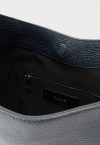 Tengerészkék bőrből készült válltáska texturált felülettel. Belsejében fekete szövettel bélelt, cipzáras zsebbel és márkajelzéssel dombornyomva.