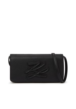 Czarna, teksturowana skórzana torba na ramię z wytłoczonymi stylizowanymi inicjałami i cienkim paskiem na ramię, przedstawiona na białym tle.