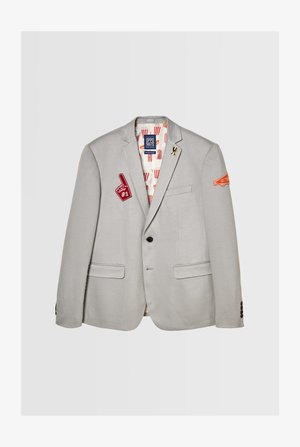 Blazer grigio con bottoni neri, due tasche frontali. Presenta toppe rosse e arancioni e un interno decorato con un design a popcorn.