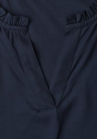 Close-up of navy blue fabric with a deep V-shaped neckline and gathered ruffle trim along the collar edges.