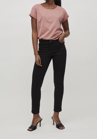 Pink short-sleeve t-shirt paired with high-waisted black skinny jeans, featuring a button closure. Black open-toe heels complete the outfit.