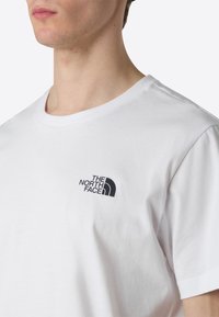 Hvid bomulds T-shirt med et sort logo af "The North Face" på venstre bryst. Korte ærmer og rund halsudskæring. Glat tekstur.