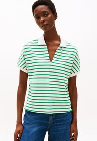 Kortermet polo skjorte, hvit med grønne horisontale striper, har V-hals og ensfarget hvit krage. Bæres med blå denim jeans.