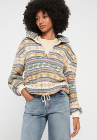 Karvane mitmevärviline pullover, millel on poollukuga kaelus, triibuline mustriga sinises, oranžis ja rohelises toonis, pehme tekstuur ja paelaga äär.