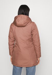 Brązowa kurtka ocieplana z kapturem, długimi rękawami i luźnym krojem. Gładka tekstura z minimalnymi detalami szwów i bez widocznych elementów metalowych.