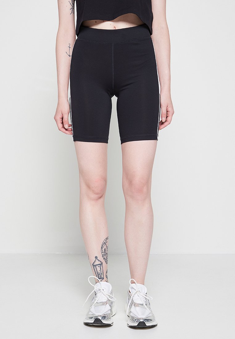 Schwarze Radshorts mit hoher Taille und glatter Textur. Verfügt über weiße seitliche Streifen und ein enges Design. Die Schuhe sind grau und weiß.