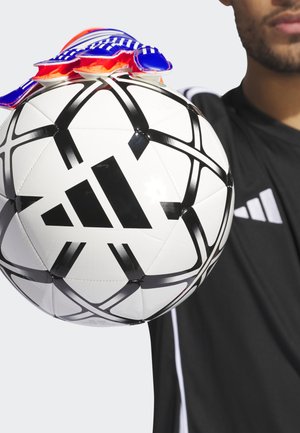 Pelota de fútbol blanca con patrones geométricos negros y un logo de Adidas, cubierta con guantes azules y rojos, sostenida por una persona con una camiseta negra.
