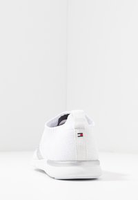 Vita stickad sneaker med grå accent på sidan, med en texturerad tyg, rund tå och logotypdetalj på hälen.