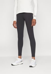 Fekete leggings elasztikus anyagból, szoros illeszkedéssel, fehér sportcipőkkel párosítva. Hosszú ujjú felső világos színben, logó részlettel.