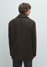 Cappotto in lana marrone con colletto a punta, silhouette dritta e cuciture minime, mostrato da dietro su uno sfondo chiaro.