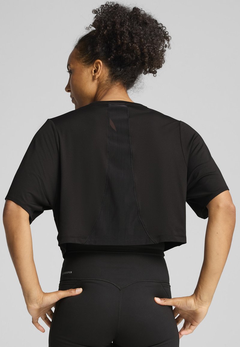 Top atletico nero corto con maniche corte, caratterizzato da un design del pannello posteriore e una texture liscia. Abbinato a leggings neri a vita alta.