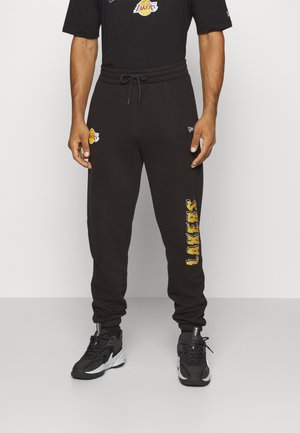 Pantalones deportivos negros con cinturilla elástica y cordón, con el texto y logotipo amarillos de "LAKERS" en el lado izquierdo. Tejido suave.