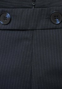 Musta pinstripe-kangas, jossa on sileä rakenne, sisältää kaksi suurta mustaa nappia ja piilotetun vetoketjusta vyötäröllä.