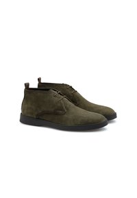 Bottines chukka en daim vert olive avec une texture lisse, présentant des accents bruns, un bout rond et une semelle en caoutchouc noir. Design à lacets.