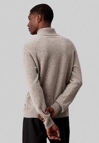 Maglione grigio chiaro con collo alto, polsini e orlo a coste. Tessuto morbido, vestibilità comoda e cuciture dettagliate lungo le giunture.