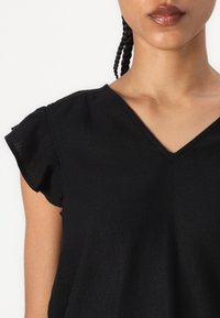 Top nero a maniche corte con scollatura a V e maniche arricciate, realizzato in un tessuto leggero e dalla texture liscia.