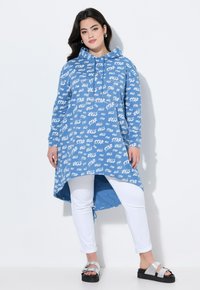 Blå huvtröja med vit "STAR" textdesign, långa ärmar, längre bakslits, matchad med vita byxor och svarta sandaler.