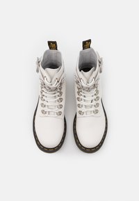 Białe skórzane botki z srebrnymi elementami i kontrastującym żółtym przeszyciem. Posiadają zaokrąglony nosek i sznurowany przód.