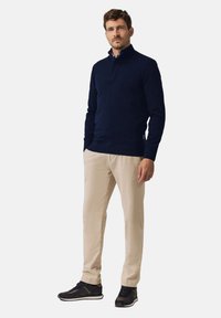 Donkerblauwe pullover met lange mouwen en een hoge kraag, gecombineerd met beige broek en zwarte sneakers. Glad stof en een ontspannen pasvorm.