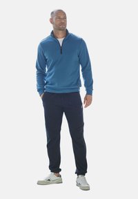 Blue fleece pullover with a zip neck, paired with black jogger pants featuring side pockets and ribbed cuffs. White low-top sneakers.