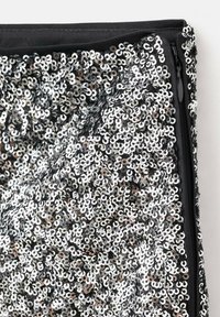 Czarna tkanina z nałożonym błyszczącym srebrnym cekinem, w kształcie okręgów. Zamek błyskawiczny widoczny po prawej stronie.