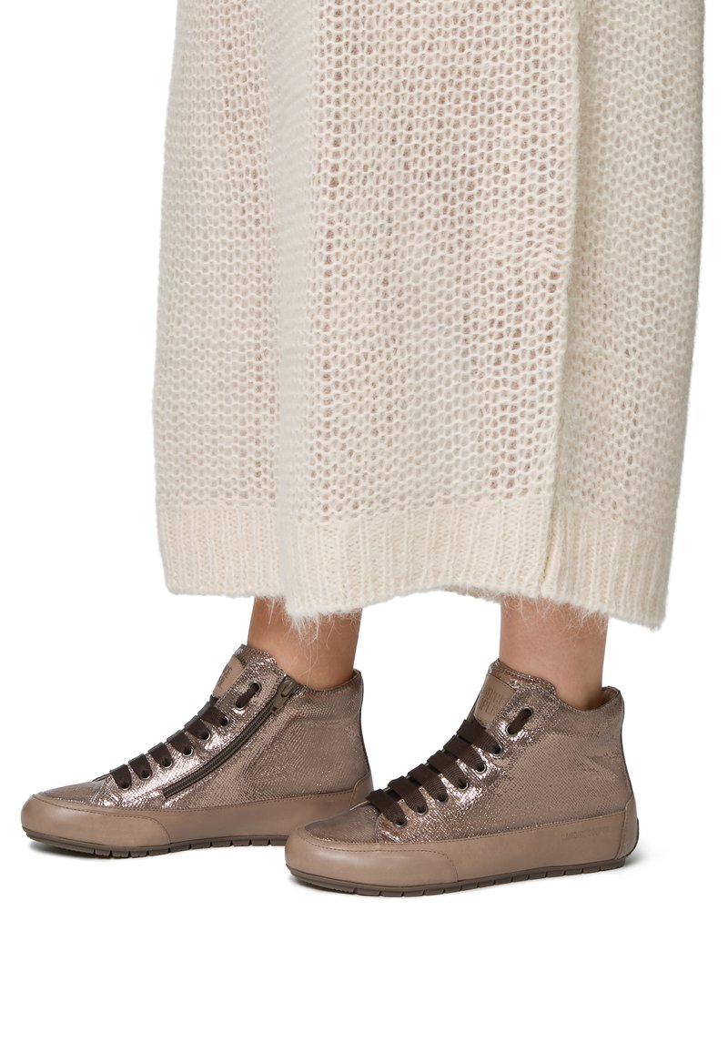 Sneaker alte in bronzo metallico con superficie texturizzata, dotate di una cerniera laterale, lacci scuri e suola in gomma, abbinate a un abito in maglia color crema.