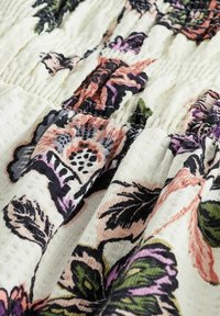 Tessuto crema con texture arricciata, caratterizzato da un motivo floreale nei toni del rosa, viola, verde e nero.