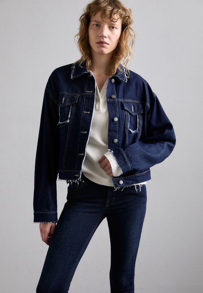 Donkerdenim cropped jack met rafelige randen, met knoopsluitingen en twee voorzakken, gecombineerd met een witte geribbelde trui en donkere jeans.