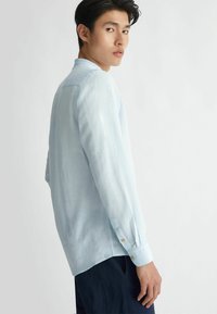 Camicia a maniche lunghe azzurro chiaro realizzata in un tessuto trasparente, con una vestibilità comoda e polsini abbottonati, caratterizzata da un'emibordo arrotondata e un design minimalista.