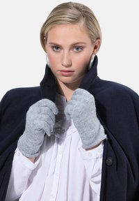 Graue gestrickte Handschuhe mit gerippter Textur, getragen von einer Person in einem dunkelblauen Mantel. Der Hintergrund ist schlicht weiß, was die Accessoires hervorhebt.