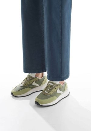 Sneakers da corsa verdi con un design a materiali misti, che includono suede e rete. Presentano dettagli in bianco e nero, e una suola spessa bianca.