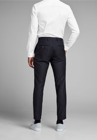 Zwarte op maat gemaakte broek met twee achterzakken en knopen; gecombineerd met een wit shirt en lichtgrijze sneakers; gladde stof en een slanke pasvorm.