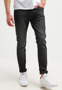Svarta smala jeans med en mjuk textur och blekt mönster, kombinerade med vita sneakers. Uppvikta byxben visar ankeln.
