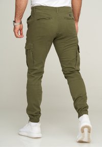 Olive green cargo pants with elastic ankle cuffs and multiple pockets, featuring a smooth texture and fitted design. Worn with white sneakers.