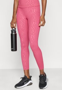 Ροζ κολάν με σχέδια από ελαστικό ύφασμα, σε συνδυασμό με μαύρα αθλητικά παπούτσια και μαύρο μπουκάλι νερού, που παρουσιάζουν κομψό σχεδιασμό.