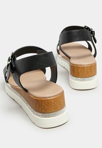 Czarne skórzane sandały z dwiema szerokimi ramiączkami, masywną drewnianą platformą i białą podstawą; posiadają rząd cyrkonii wzdłuż platformy.