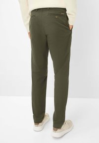 Olivengrønne chinos med tapered ben, to baglommer og knaplukning. Båret med beige sneakers, der har et enkelt design og glat tekstur.