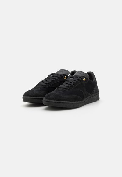 Black suede sneakers with a rubber sole, round toe, flat laces, and gold metal accents on the eyelets. Textured upper with stitching details.