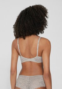 Lace bra in light gray, featuring adjustable straps, a hook-and-eye closure, and floral patterns. Smooth, delicate texture.