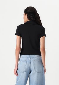 Svart kortärmad polo med krage, figursydd design. Kombinerad med högmidjade ljusblå vida jeans med bakfickor.