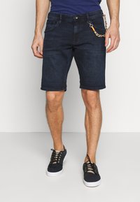 Donkerblauwe denim shorts met een standaard pasvorm, omgerolde zoom, vijf zakken en een decoratieve ketting bevestigd aan de voorkzak.
