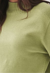 Grüner gestrickter Pullover mit geripptem Ausschnitt. Der Stoff hat eine weiche Textur, zeigt die Stiche und hat eine lockere Passform an den Schultern.