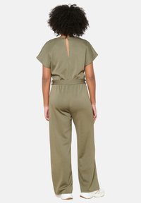 Oljčno zelena kombinezonska obleka s kratkimi rokavi, podrobnostjo v obliki ključavnice na hrbtu, pasom z zanko in širokimi hlačami, narejena iz mehke, teksturirane tkanine.