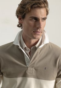 Camisa de rugby beige y blanco roto con un colorido contraste en el cuello y un logo bordado en el pecho. Tejido suave con un acabado texturizado.