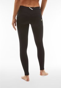 Leggings neri realizzati in tessuto elasticizzato con vita alta, dotati di tasche posteriori e cuciture visibili. Il design segue la forma del corpo.