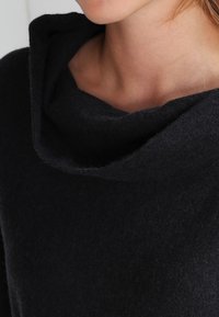 Maglione nero con collo a cowl morbido, caratterizzato da una vestibilità comoda e un tessuto testurizzato. Vista ravvicinata che evidenzia il collo e la qualità del materiale.